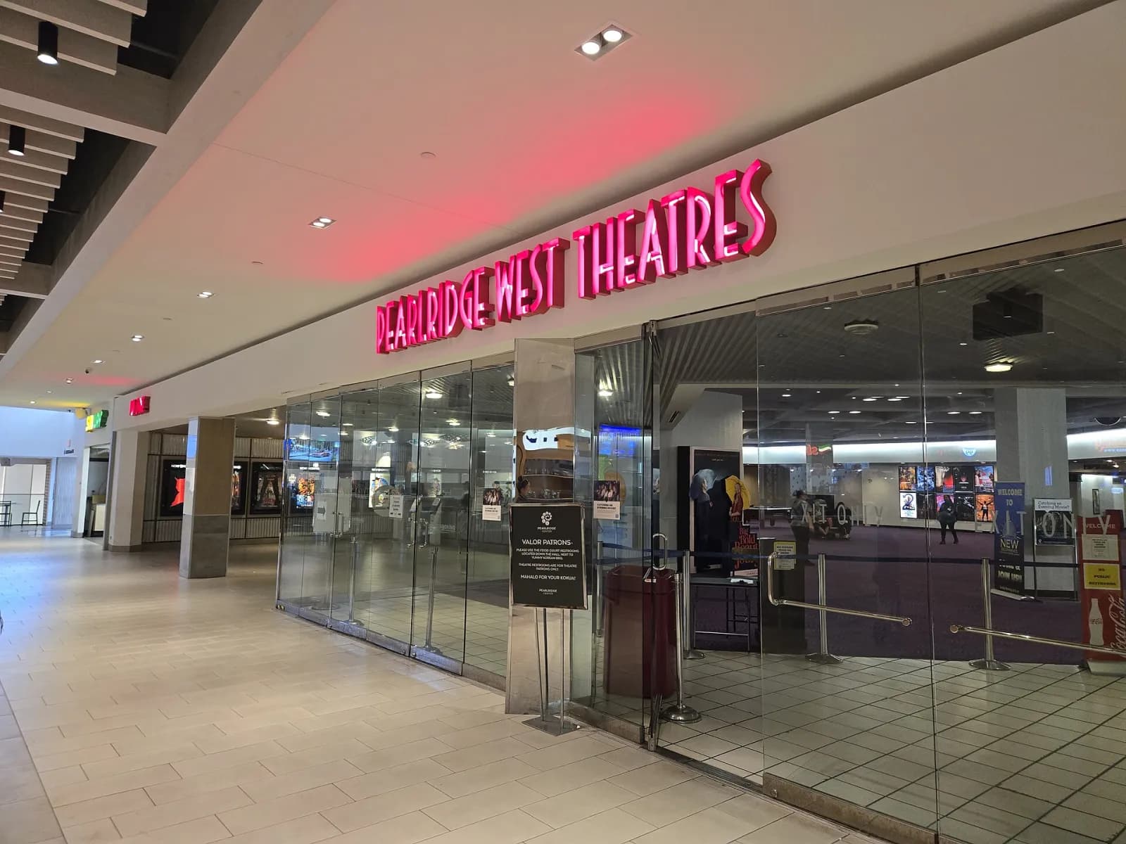 Hành lang bên trong Pearlridge Center với sàn gạch sáng và lối vào rạp chiếu phim có bảng đèn hồng (ảnh chụp tháng 9 năm 2025)